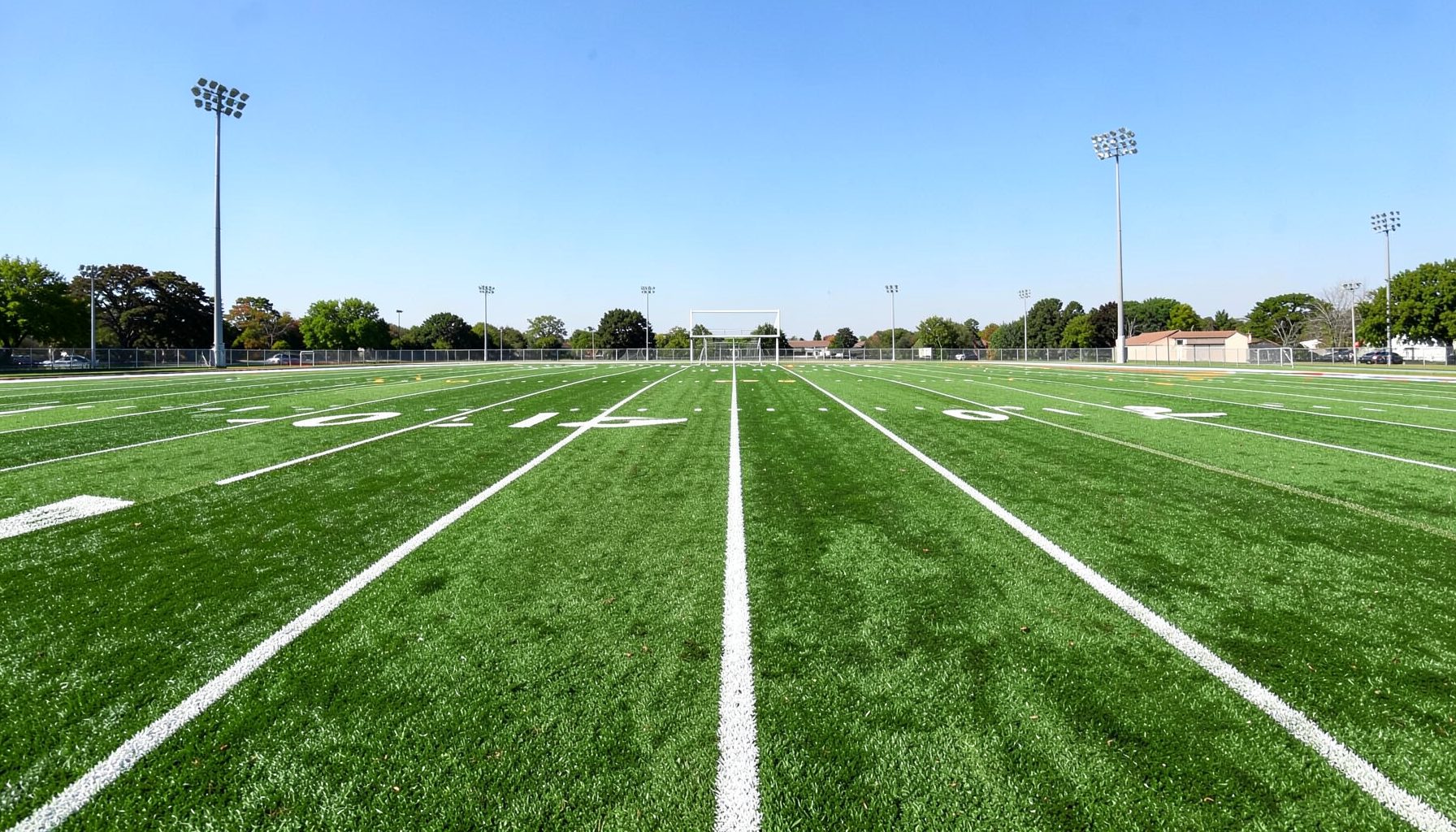 A green football field with white yard lines stretching toward an end zone under a bright afternoon sky.