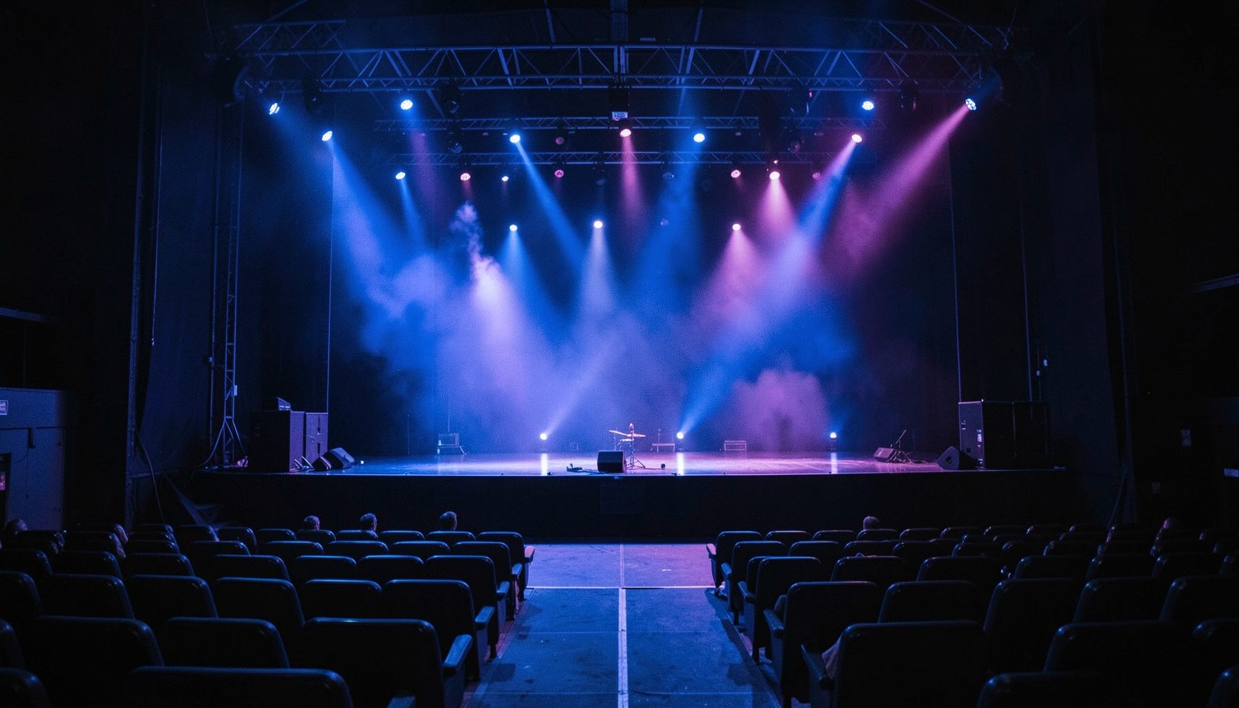 Concert stage with dramatic blue and purple lighting, empty seats in the foreground, moody atmosphere
