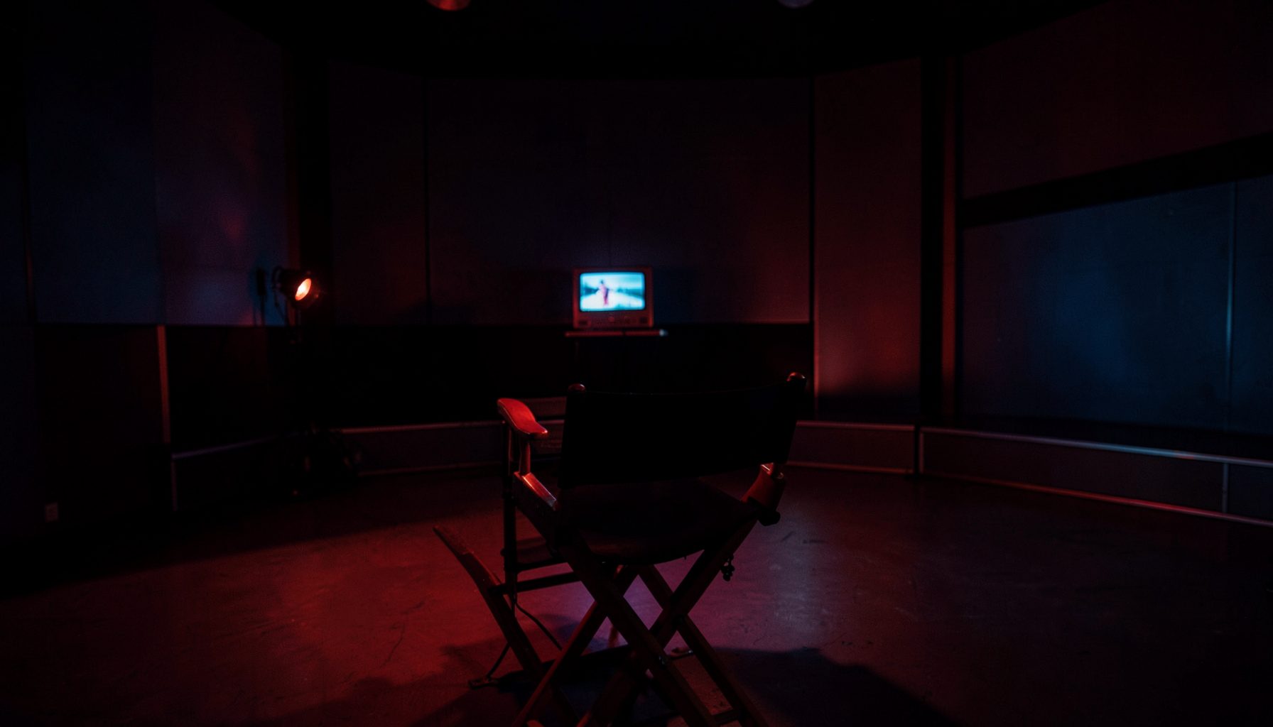 Dark room with a single director's chair facing a small glowing television screen, red and blue cinematic lighting