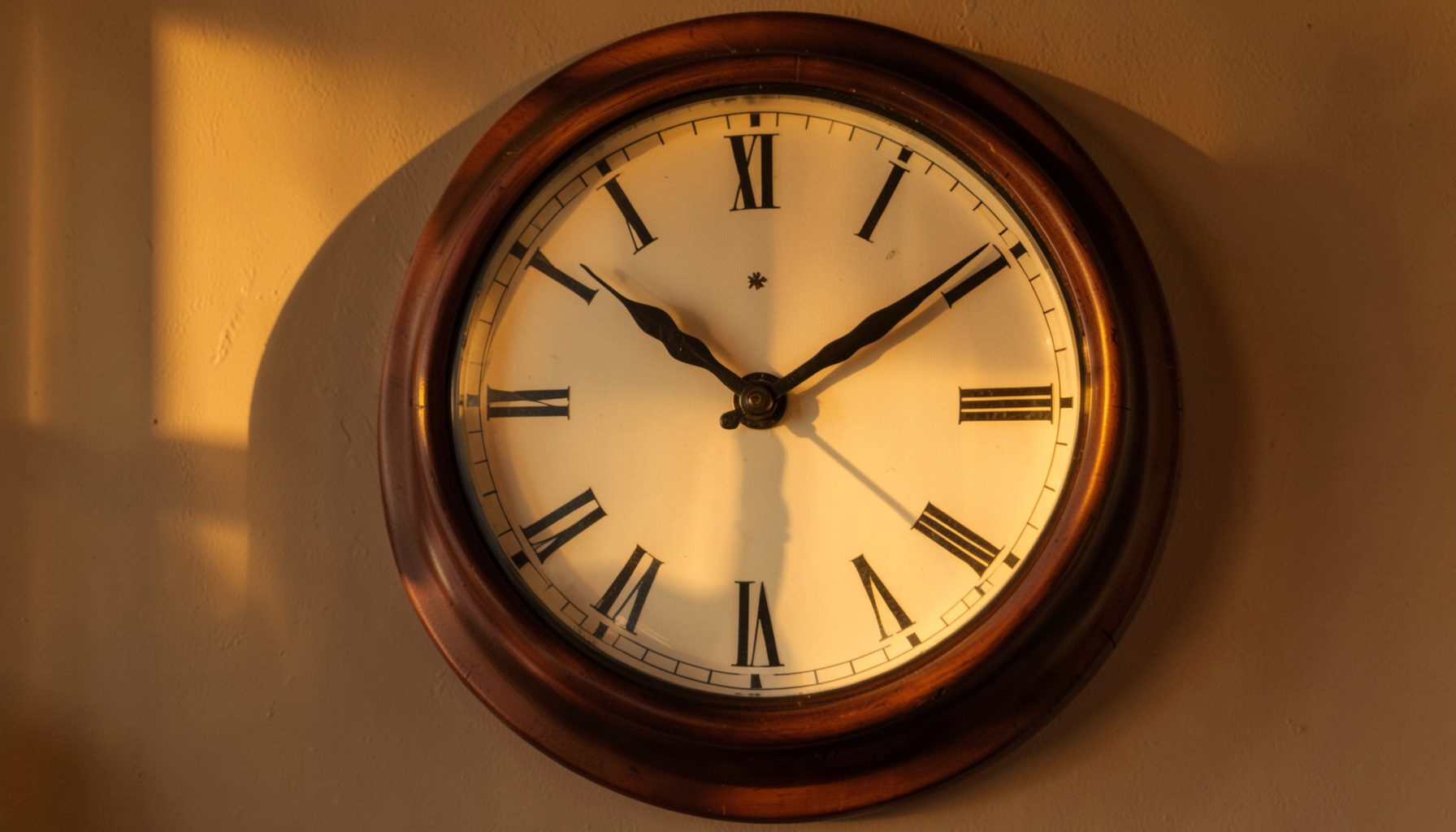 Wooden-framed analog wall clock with Roman numerals lit by warm sunlight, suggesting the passage of market time.