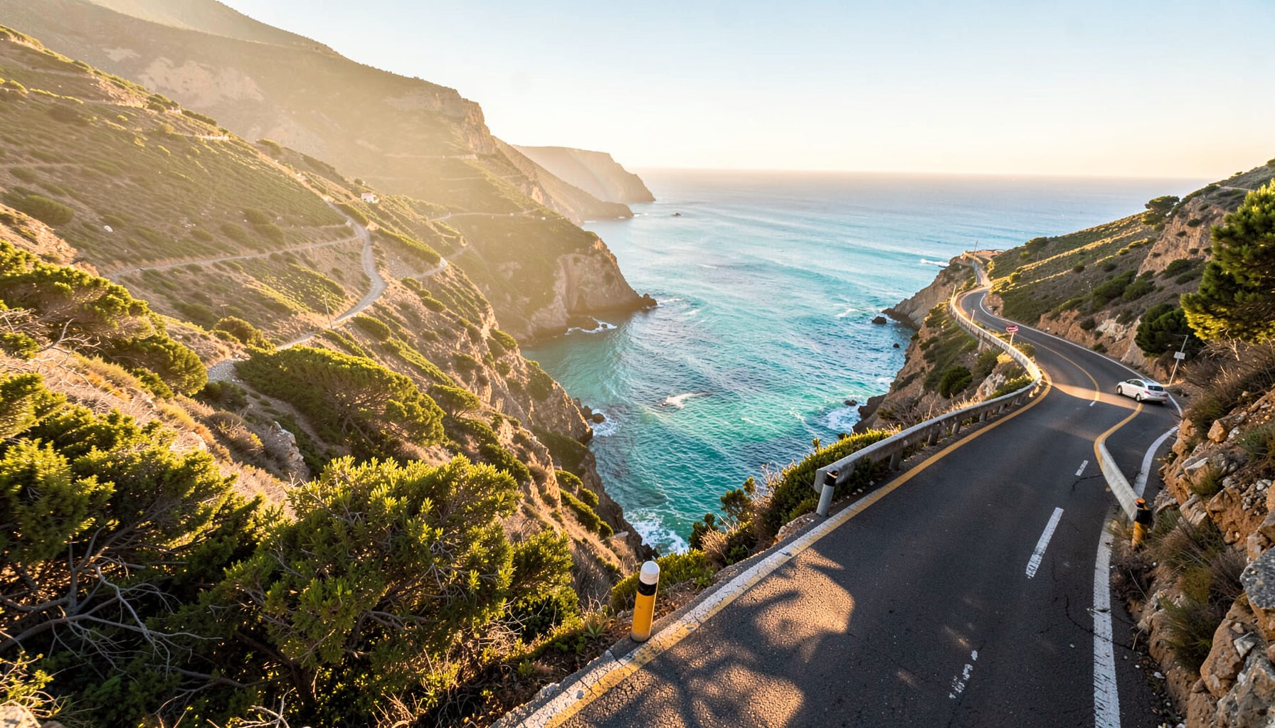 Winding coastal road along cliffs overlooking turquoise ocean at sunrise