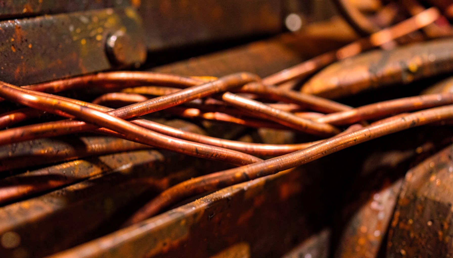 Close-up of tangled copper pipes and wires on a rusted metal surface, warm orange and brown industrial tones
